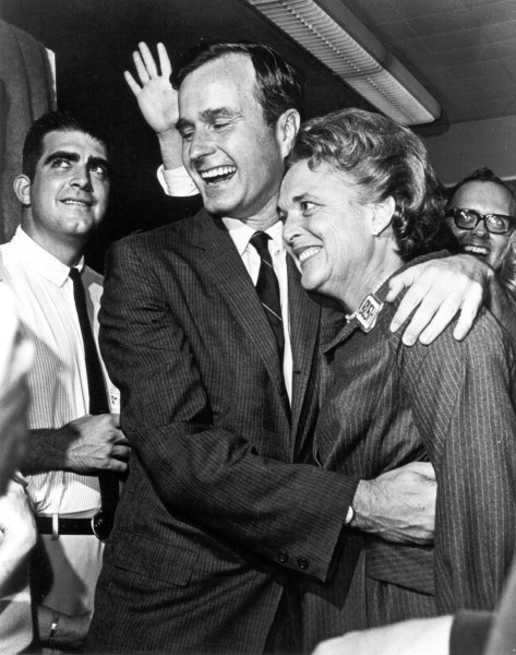Photographic print of George Bush embracing Barbara Bush, both smiling, as he waves to a crowd of onlookers behind them