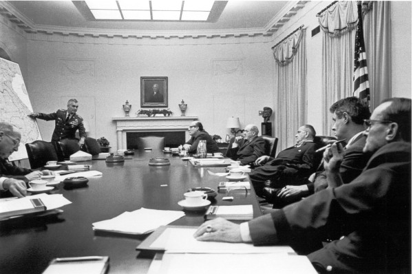 Photographic print of General Westmoreland pointing to a large map on an easel while six men in suits and military uniform sit around a long conference table in the White House Cabinet Room