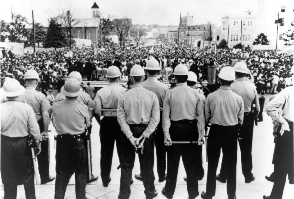 Photographic print of helmeted Alabama state agents standing in a row on capitol steps, backs to camera, facing a massive crowd filling the street below