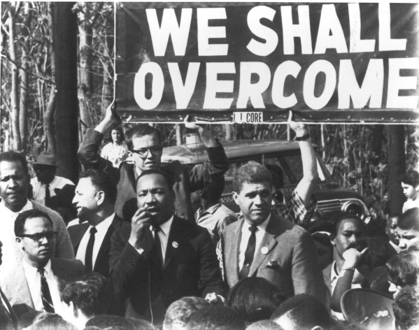 Photographic print of Dr. Martin Luther King Jr. addressing a crowd at a civil rights demonstration, with a large "We Shall Overcome" banner held overhead