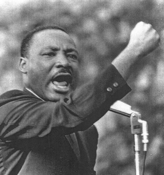 Photographic print of Martin Luther King, Jr. speaking passionately at a microphone, mouth open wide and right fist raised overhead