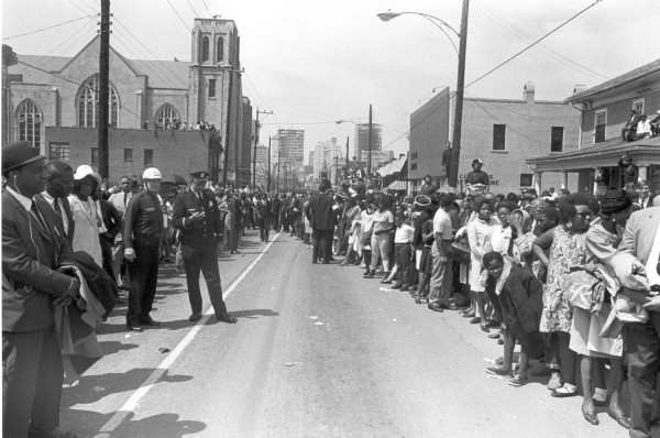 Photographic print of a large crowd lining both sides of an Atlanta street, with uniformed police officers standing in the cleared roadway. A Gothic-style church and city skyline are visible in the background