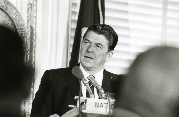 Photographic print of Ronald Reagan speaking at a podium with microphones, a partial "NATIO" nameplate visible in the foreground and a National Press Club seal to the left