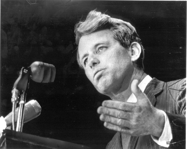Photographic print of Senator Robert F. Kennedy speaking at a podium with microphones, gesturing with one hand against a dark background
