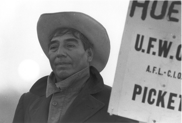 Photographic print of a man in a cowboy hat and jacket standing beside a U.F.W.O.C. AFL-CIO picket sign reading "HUELGA"