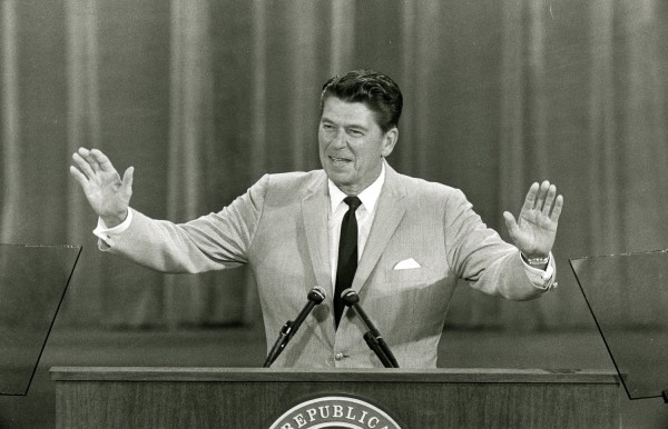 Photographic print of Ronald Reagan speaking at a podium with two microphones, arms outstretched, wearing a suit and tie. A partial Republican National Committee seal is visible on the lectern