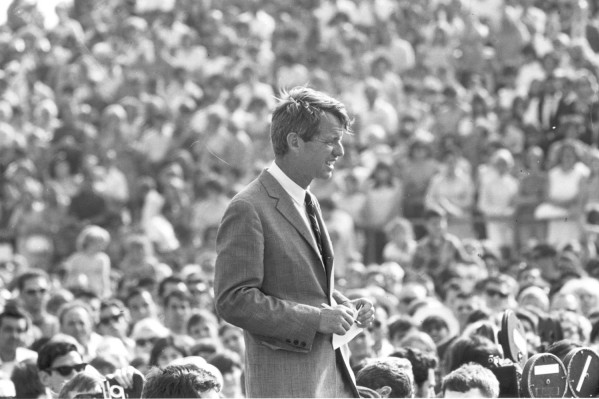 Photographic print of Robert F. Kennedy in a suit and tie, holding papers, standing before a massive outdoor crowd packed densely behind him