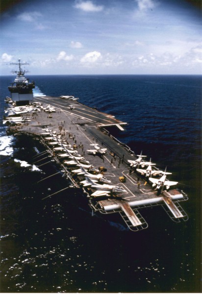 Photographic print of USS Enterprise (CVAN-65) seen from above, its flight deck lined with A-4 Skyhawk aircraft as it cruises through dark blue open water