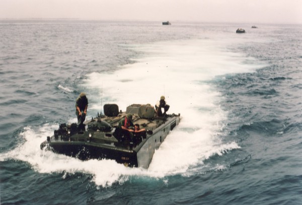 Photographic print of an amtrac cutting through open water with several personnel on deck, with two additional amtracs visible in the background