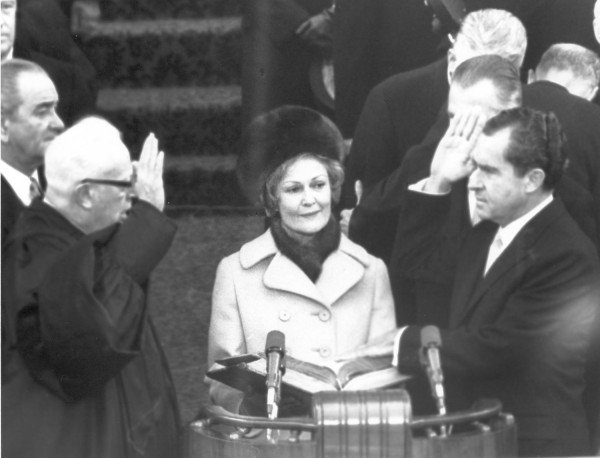 Photographic print of Richard Nixon raising his right hand at a podium while Justice Earl Warren administers the oath, with Pat Nixon standing between them holding a Bible