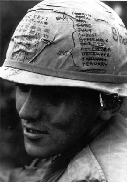Photographic print of a soldier in close profile wearing a cloth-covered helmet marked with months, crossed-out dates, countdown numbers, and the words "Short" and "Days Left Viet-Nam"