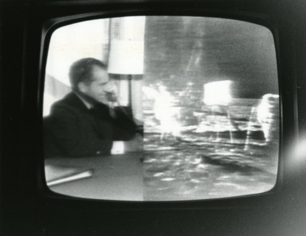 Photographic print of a television screen displaying a split black-and-white broadcast of President Nixon on the phone and astronauts on the lunar surface