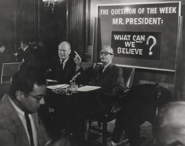 Photographic print of Congressman Ford and Senator Dirksen seated at a table with microphones, beside a sign reading "The Question of the Week Mr. President: What Can We Believe?"