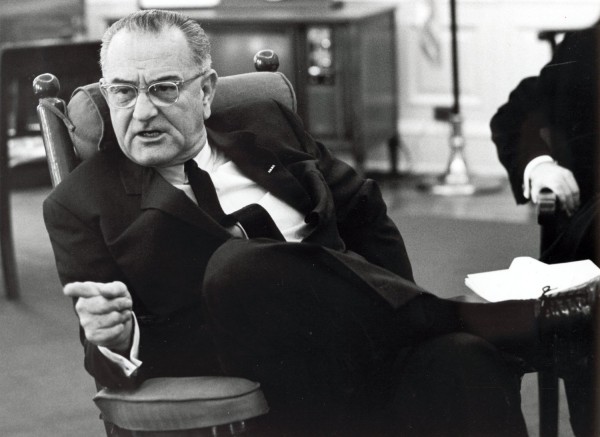 Photographic print of Lyndon B. Johnson seated in a chair in the Oval Office, leaning back and pointing his finger while speaking