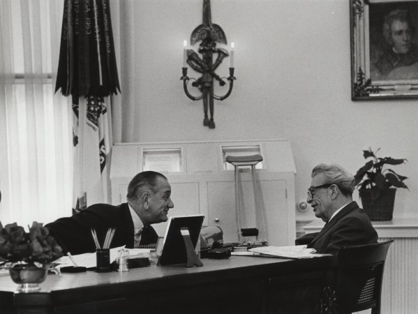 Photographic print of LBJ and Senator Dirksen laughing across a large desk in the Oval Office, with flags, a wall sconce, and a portrait visible behind them
