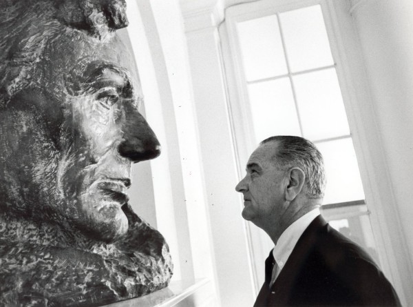 Photographic print of President Lyndon Johnson in profile, gazing intently at a large bronze bust sculpture of Abraham Lincoln near a window
