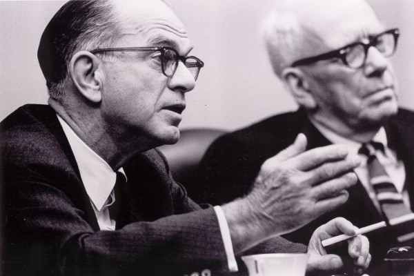 Photographic print of Senators Fulbright and Aiken seated at a table, Fulbright speaking and holding a cigarette, Aiken in soft focus behind him