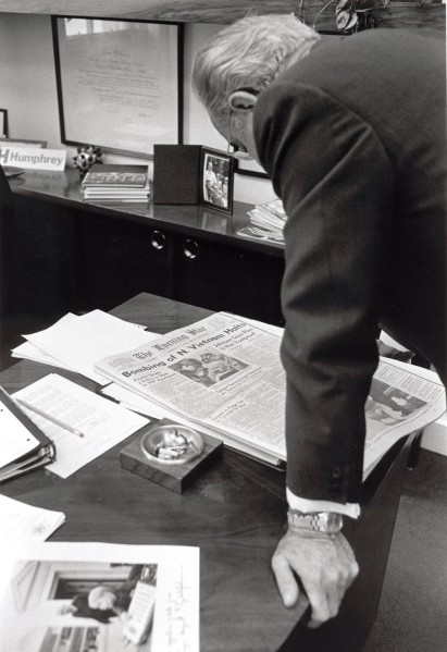 Photographic print of President Lyndon B. Johnson leaning over a desk to read The Evening Star, its front page headline reading "Bombing of N. Vietnam Halts"