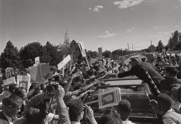 Photographic print of Lyndon B. Johnson leaning over a convertible to reach a massive crowd of outstretched arms holding "Welcome President Johnson" signs