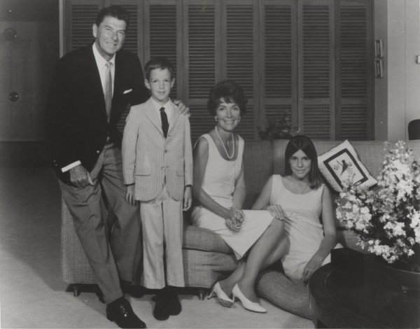 Photographic print of the Reagan family — two adults and two children — posing in a living room with a floral arrangement and louvered doors behind them