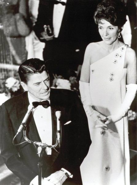 Photographic print of Ronald Reagan in a tuxedo speaking at a microphone podium while Nancy Reagan stands beside him in a formal gown