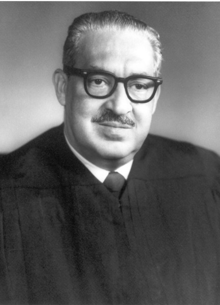 Photographic print portrait of Thurgood Marshall wearing black judicial robes, a tie, and thick-framed glasses against a neutral gray background