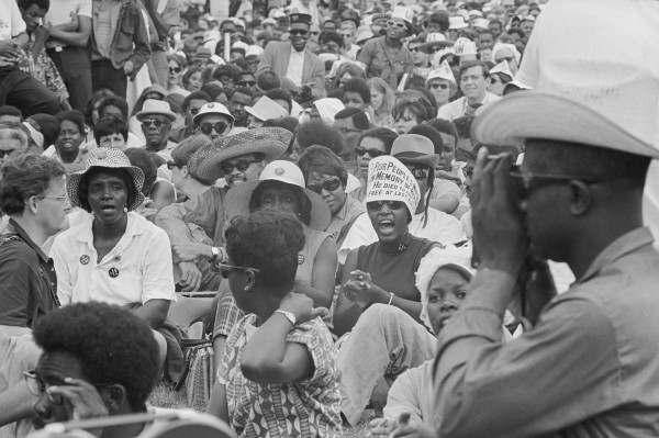 Black-and-white photograph of a dense outdoor crowd; one woman wears a hat bearing text reading 'Poor People's March — In Memory of — He Died to — Free at Las—'