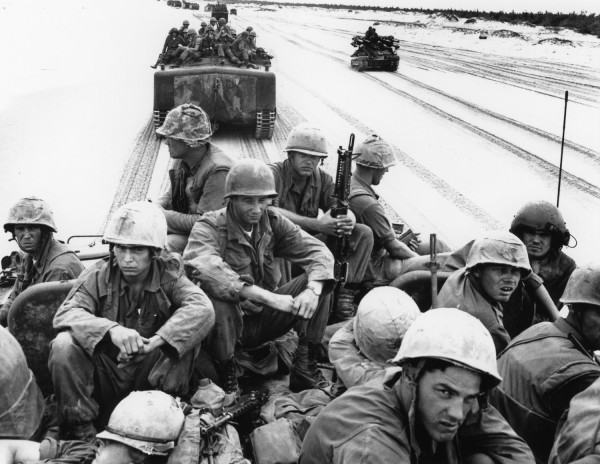 Gelatin silver print of helmeted soldiers seated atop a large tracked amphibious vehicle crossing a sandy terrain, with additional vehicles visible behind