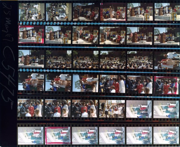 Color contact sheet of roughly 30 frames from an outdoor dedication ceremony, showing a stage with speakers at a podium, a large seated crowd, and small-group interactions among attendees